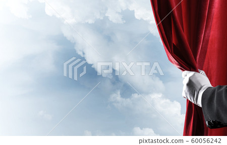 Cloudy landscape behind red curtain and hand holding it 60056242