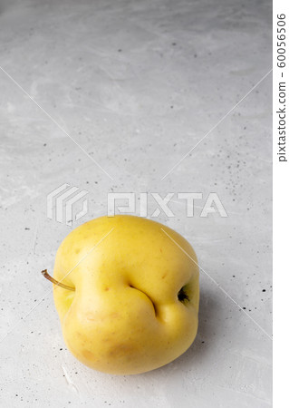 Single ugly yellow apple with dent on grey concrete background. Waste zero concept. Close-up, copy space, perspective view. Single ugly yellow apple with dent on grey concrete background. Waste zero concept. Close-up, copy space, perspective view. 60056506