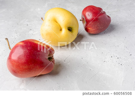 Three ugly red and yellow apples are lying chaotically on grey concrete background. Waste zero concept. Image with copy space. Three ugly red and yellow apples are lying chaotically on grey concrete background. Waste zero concept. Image with copy space. 60056508