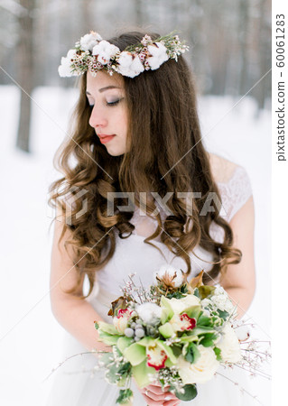 Portrait of a beautiful young woman, bride, in a winter forest. Bride with wreath on the head, made from cotton, holding winter bouquet Portrait of a beautiful young woman, bride, in a winter forest. Bride with wreath on the head, made from cotton, holding winter bouquet 60061283