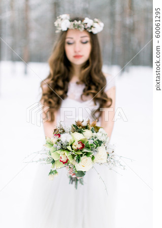 Winter wedding flower bouquet with cotton. Young and beautiful bride with the flower bouquet in winter forest. Focus on the bouquet 60061295