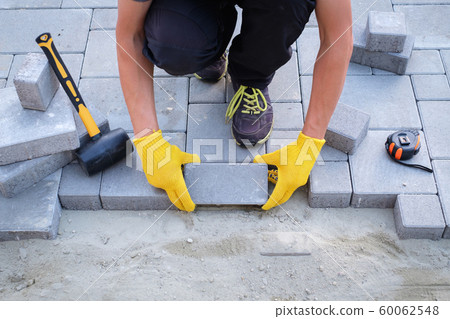 The master in yellow gloves lays paving stones 60062548