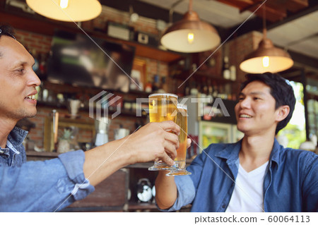 Two young men colliding with two glass of beer to 60064113