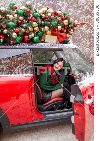 Pretty young girl is sitting in red car with decorated xmas tree on the roof. Pretty young girl is sitting in red car with decorated xmas tree on the roof. 60065530