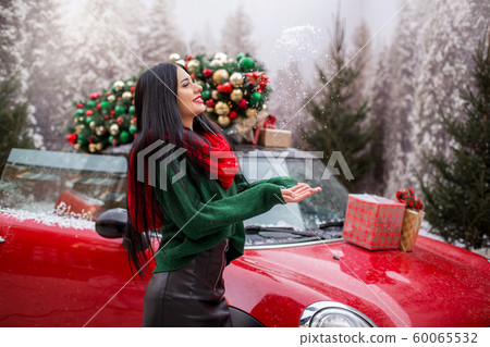 Pretty young girl is playing with snow near red car with decorated xmas tree. Pretty young girl is playing with snow near red car with decorated xmas tree. 60065532
