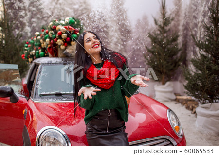 Pretty young girl is playing with snow near red car with decorated xmas tree. Pretty young girl is playing with snow near red car with decorated xmas tree. 60065533