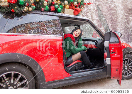 Pretty young girl is sitting in red car with decorated xmas tree on the roof. Pretty young girl is sitting in red car with decorated xmas tree on the roof. 60065536