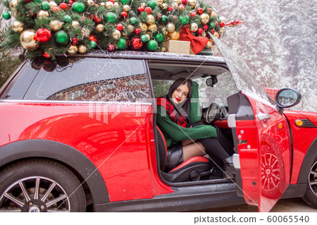 Pretty young girl is sitting in red car with decorated xmas tree on the roof. xmas concept. Pretty young girl is sitting in red car with decorated xmas tree on the roof. xmas concept. 60065540