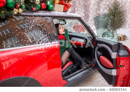 Pretty young girl is sitting in red car with decorated xmas tree on the roof. xmas concept. Pretty young girl is sitting in red car with decorated xmas tree on the roof. xmas concept. 60065541