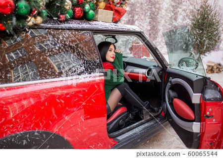 Pretty young girl is sitting in red car with decorated xmas tree on the roof. xmas concept. Pretty young girl is sitting in red car with decorated xmas tree on the roof. xmas concept. 60065544
