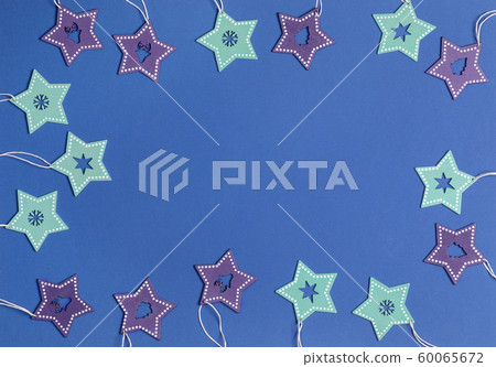 Xmas decoration. Festive blue background with frame of Christmas toys painted wooden turquoise and purple stars with carved in them deers, Christmas trees, snowflakes, stars. Flat lay, copy space. Xmas decoration. Festive blue background with frame of Christmas toys painted wooden turquoise and purple stars with carved in them deers, Christmas trees, snowflakes, stars. Flat lay, copy space. 60065672