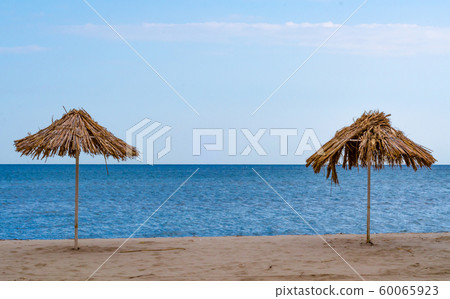 damaged two straw beach umbrellas on an empty seashore on a clear day 60065923