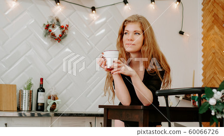 Woman holds a cup of coffee in the morning in Christmas kitchen Woman holds a cup of coffee in the morning in Christmas kitchen 60066726