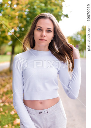 Beautiful and stylish woman in autumn portrait, resting and smiling, warm casual clothes, long hair, trees road background, yellow brown leaves. Emotions tenderness and positive. 60070039