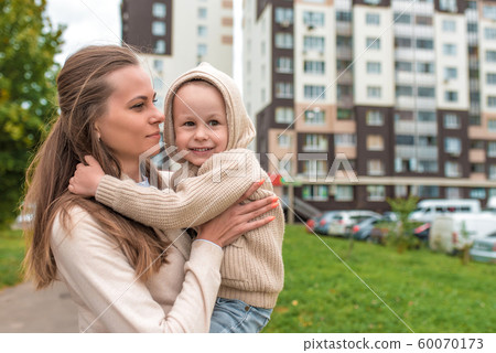 Young happy family, woman mom and little son boy. Hug in autumn on street, smiling for a walk and rejoice. Casual warm clothes with a hood jumper. Free space for copy text. 60070173