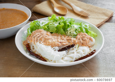 close up of rice noodles with fish curry sauce in a ceramic dish on wooden table. close up of rice noodles with fish curry sauce in a ceramic dish on wooden table. 60078697