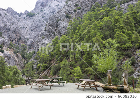 Recreation area with wooden tables and  wooden drinking water tank in gorge among mountains and green pine forest. Selective focus. 60082016