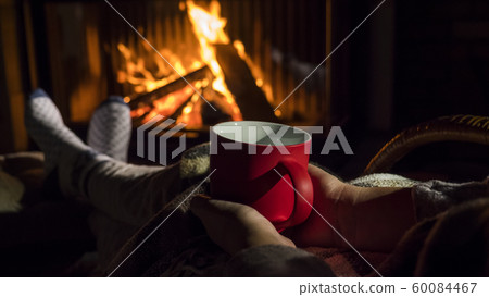 Woman with a red cup of tea is relaxing by the fireplace 60084467