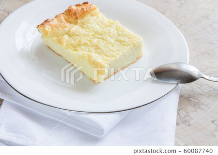 Piece of curd casserole on white plate on wooden cut. Classic recipe contains: cottage cheese, eggs, sour cream, semolina, butter, sugar. Selective focus. 60087740