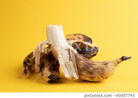 Close-up one peeled banana and two unpeeled overripe blackened ugly bananas on bright yellow background. Zero waste concept. 60087743
