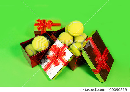 Tennis balls in holiday gift red boxes as present for Christmas, New Year, birthday on green color Tennis balls in holiday gift red boxes as present for Christmas, New Year, birthday on green color 60090819