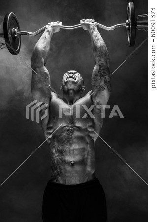 Strong sportsman lifting heavy dumbbell in smoke Strong sportsman lifting heavy dumbbell in smoke 60091373