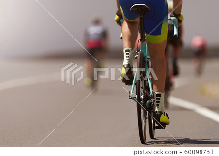 Cycling competition cyclist athletes riding a race at high speed, detail on gear wheels and feet Cycling competition cyclist athletes riding a race at high speed, detail on gear wheels and feet 60098731