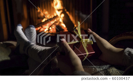 Woman holds a box with a gift in her hands, sits near the fireplace 60100437