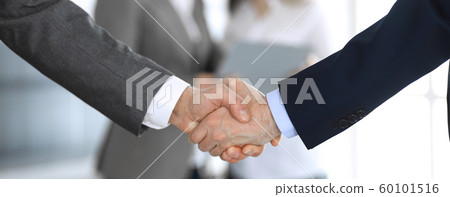 Business people shaking hands while standing with colleagues after meeting or negotiation, close-up. Group of unknown businessmen and women in modern office. Teamwork, partnership and handshake 60101516
