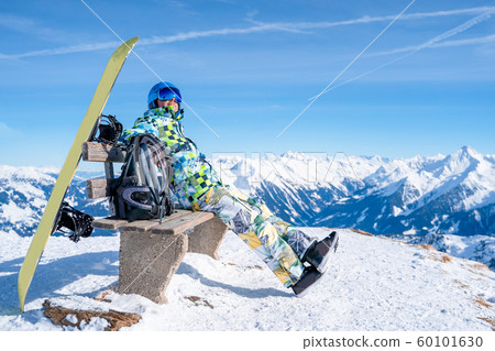 Photo from side of athlete man sitting on bench next to snowboard in ski resort. Photo from side of athlete man sitting on bench next to snowboard in ski resort. 60101630
