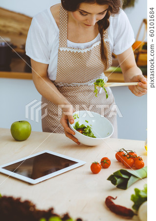 Young brunette woman cooking in kitchen. Housewife holding wooden spoon in her hand. Food and health concept 60101684