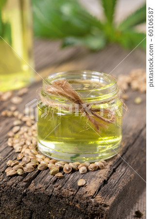 Hemp CBD oil in glass jar and grains of cannabis on old wooden board, bottle with oil and leaves are blurred on backdrop. Natural products concept. Hemp CBD oil in glass jar and grains of cannabis on old wooden board, bottle with oil and leaves are blurred on backdrop. Natural products concept. 60106587