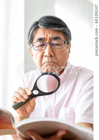 Senior man reading with magnifying glass 60109247