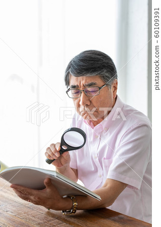Senior man reading with magnifying glass 60109391