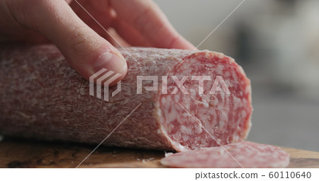 man slicing salame sausage on olive wood board 60110640