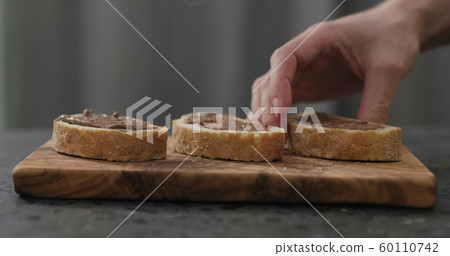 man take ciabatta slice with chocolate nut butter on olive board man take ciabatta slice with chocolate nut butter on olive board 60110742