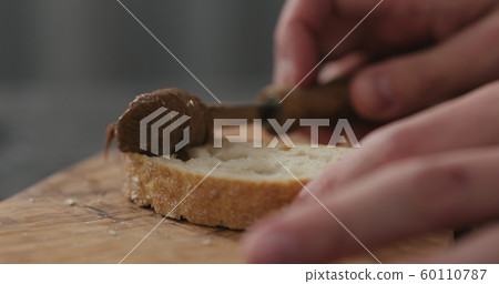 man spreading chocolate nut butter on ciabatta slice on olive board 60110787
