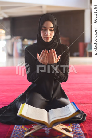 Young muslim woman in wear black dress praying with quran in mosque. 60111263