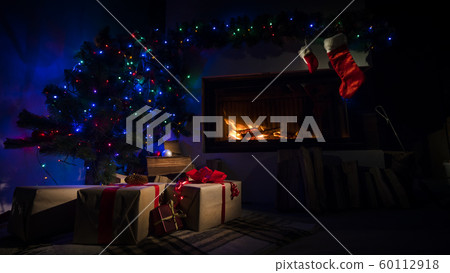 Room in the twilight with a fireplace and a Christmas tree with Christmas presents Room in the twilight with a fireplace and a Christmas tree with Christmas presents 60112918