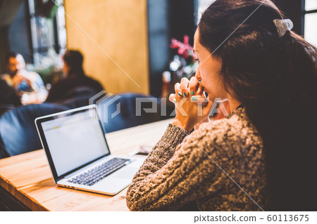 beautiful young brunette girl in sweater working on laptop computer inside cafe at wooden table near window. Winter and Christmas decorations. beautiful young brunette girl in sweater working on laptop computer inside cafe at wooden table near window. Winter and Christmas decorations. 60113675
