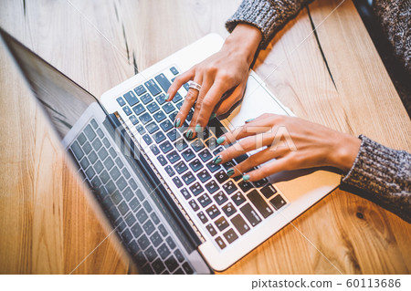 Close-up of a young girl's hand in a gray sweater use laptop technology on a wooden table in a cafe. Near the mobile phone and glasses. The concept of remote work business lady. 60113686