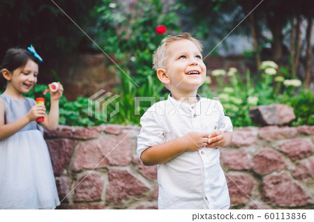 Two children in the park blowing soap bubbles and having fun. Two baby Playing With Soap Bubbles. brother and sister having fun outdoors, happy childhood concept Two children in the park blowing soap bubbles and having fun. Two baby Playing With Soap Bubbles. brother and sister having fun outdoors, happy childhood concept 60113836