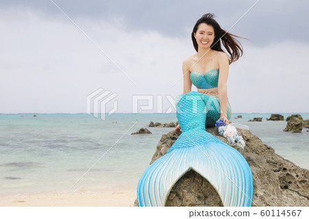坐在海邊的岩石上的微笑美人魚 60114567