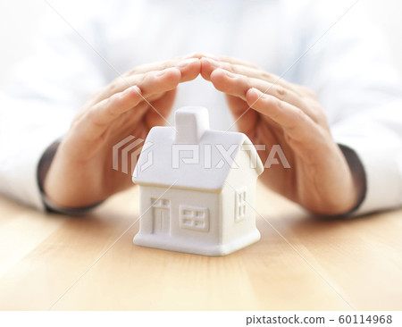Small white toy house protected by hands 60114968