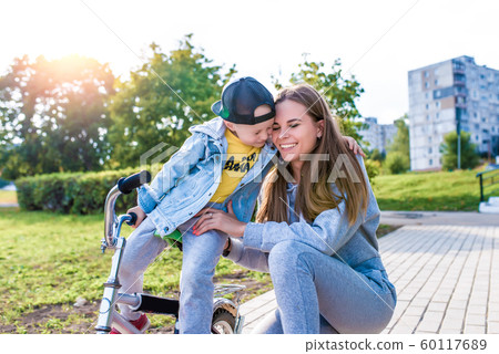 Family mother woman little boy son 3-5 years old, summer city, learns to ride bicycle, plays laughing fun, emotions joy relaxation weekend. Everyday clothes, parenting support care for child. 60117689