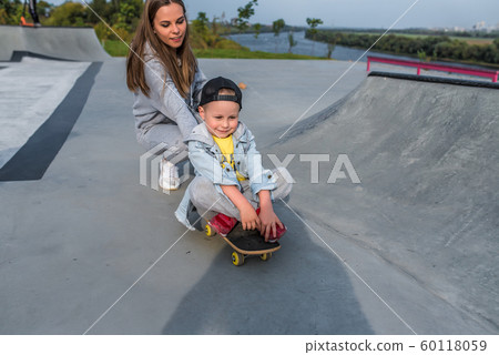 Family mother woman little boy son 3-5 years old, summer sports field in city, playing skateboarding, emotions of joy, fun relaxation on weekend. Everyday clothes, parenting support care for child. 60118059