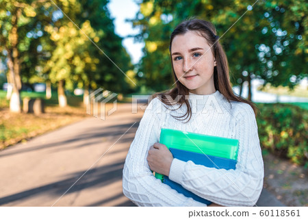 Teenager girl 14 years old autumn day summer city, hands notebooks folders with notes, happy smiling smart student, serious successful, sweater, outdoors portrait teenager schoolgirl. Free space text 60118561