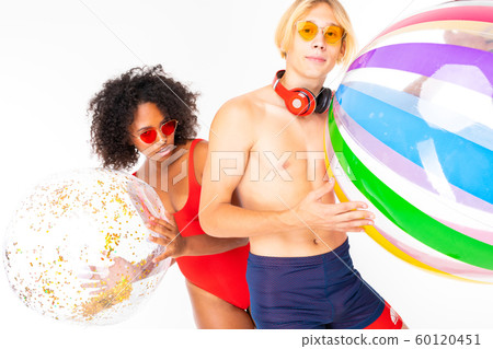 African female and caucasian blonde man stands in swimsuit with big rubber balls and smiles African female and caucasian blonde man stands in swimsuit with big rubber balls and smiles 60120451