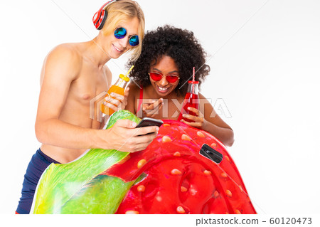 Pretty african female and caucasian blonde man stands in swimsuit with rubber beach mattresses Pretty african female and caucasian blonde man stands in swimsuit with rubber beach mattresses 60120473