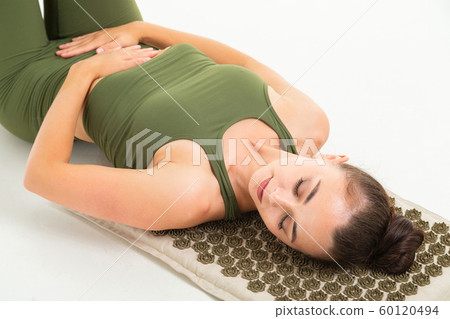 European brunette girl in a green sports suit meditates lying on a massage mat on a white background European brunette girl in a green sports suit meditates lying on a massage mat on a white background 60120494